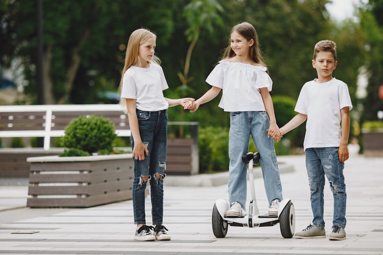 Three children holding hands, one on a segway, enjoying a playful day in an urban outdoor park.